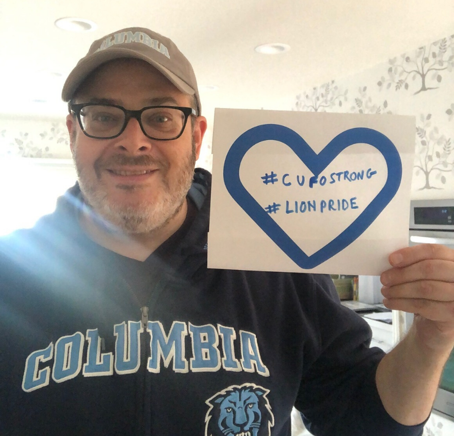 A man wearing a Columbia-branded zip-up hoodie holds a handmade sign that says, "#CUFO Strong, #Lion Pride"