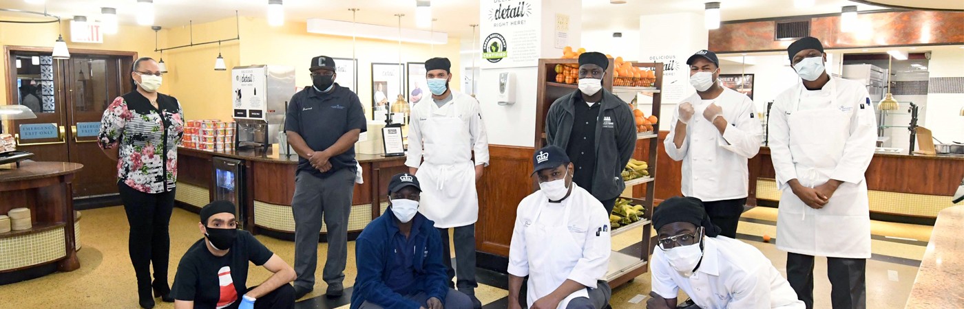 Members of the Columbia Dining team stand inside John Jay Dining Hall wearing masks.