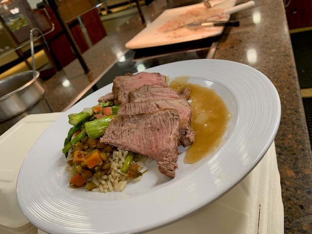 A plate of prime rib on a bed of rice and vegetables sits on the Dining Hall counter with a carving board in the background.