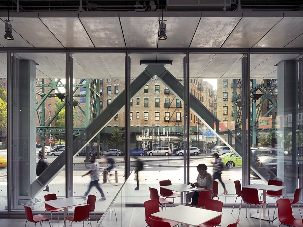 The ground floor of The Forum offers space for public use and includes a cafe, spacious seating, and free Wi-Fi. (Photo: Nic Lehoux) The interior of the ground floor of The Forum, with a person sitting down at one of the tables and people seen walking outdoors.