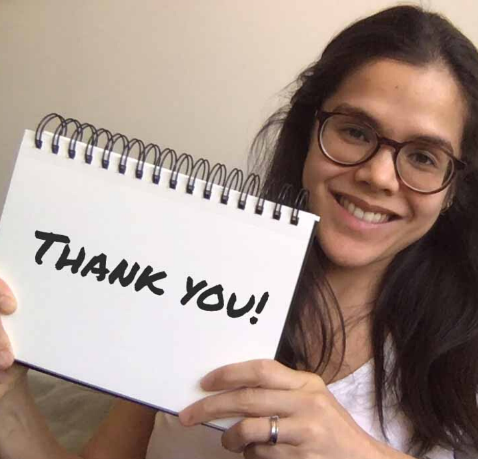 A woman with glasses holds up a notebook that says, "Thank you"