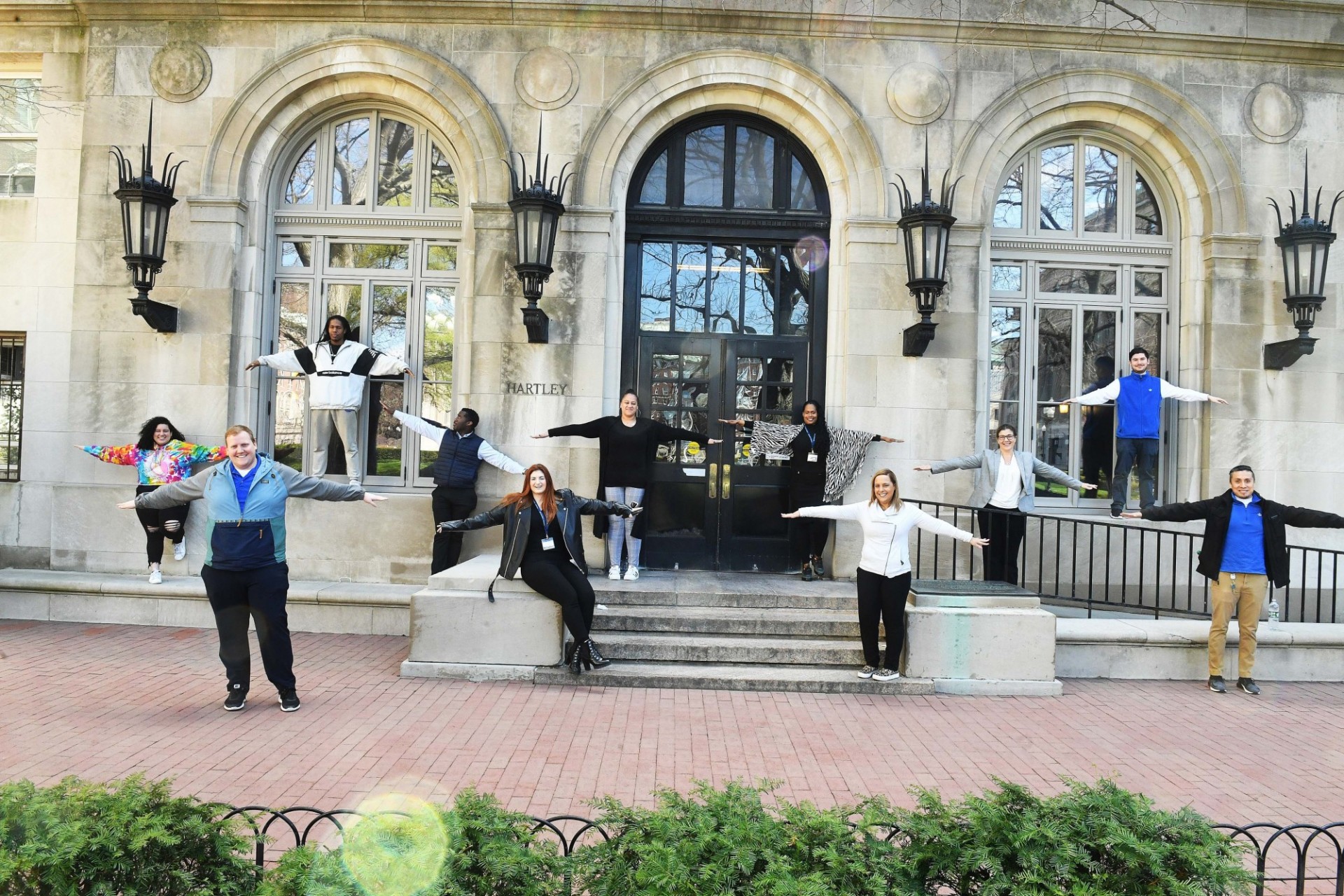 The Housing team stands six feet apart with their arms spread out, in front of Hartley Hall.