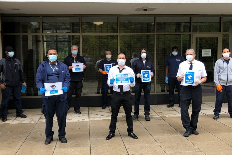 The Columbia Residential team that supports the residents at 560 Riverside Drive. A group of Columbia Residential employees stand outside of a building entrance that is covered with windows.