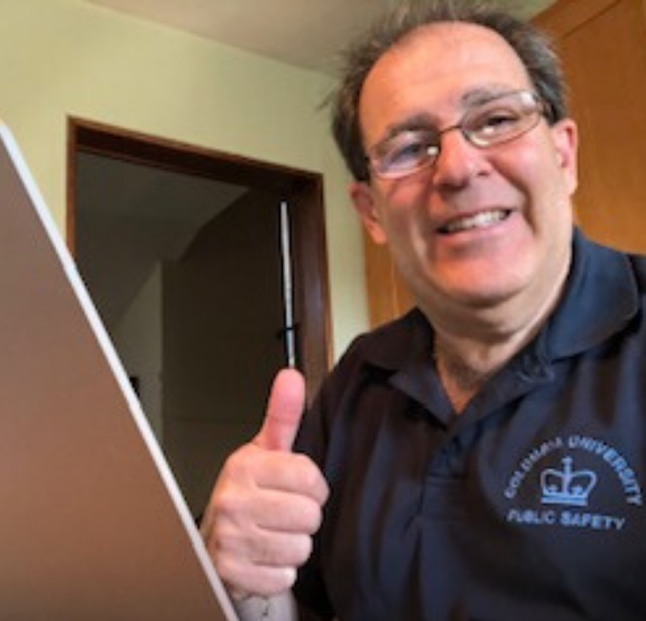 A person with glasses facing a laptop giving a thumbs-up sign.