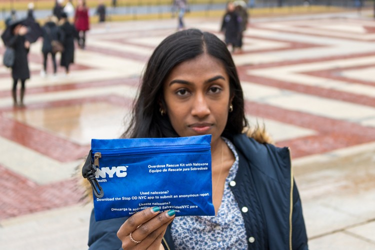 A woman on Low Plaza is holding a blue naloxone kit up to the camera.