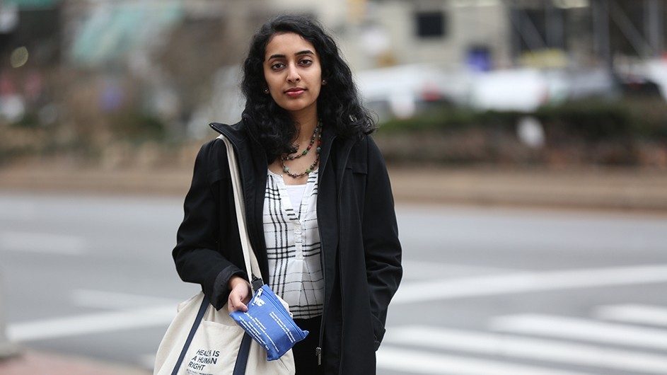 A woman stands on a sidewalk, holding a naloxone kit.