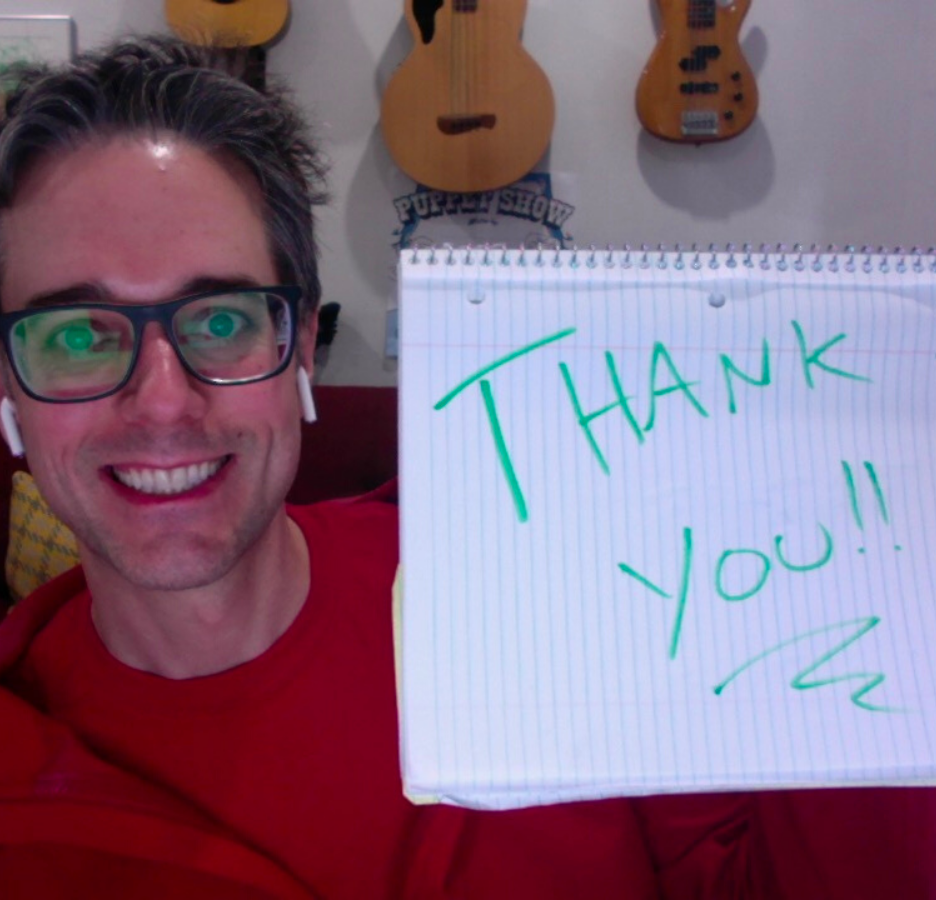 A person with glasses and a red shirt holds up a homemade sign that says "Thank You"