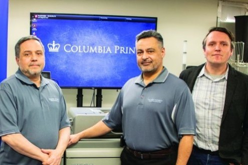Columbia Print team leaders standing in front of a printer with a blue Columbia Print sign in the background.
