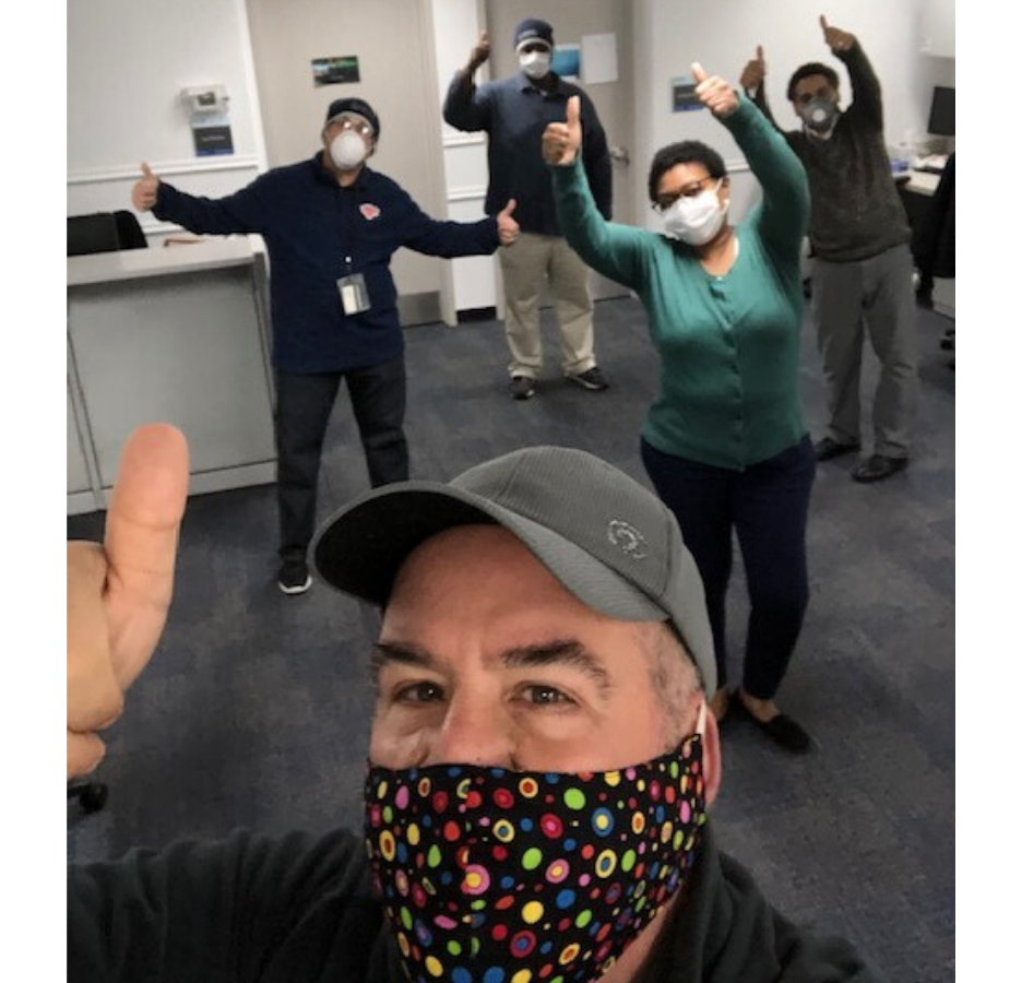 A group poses in an office with thumbs up