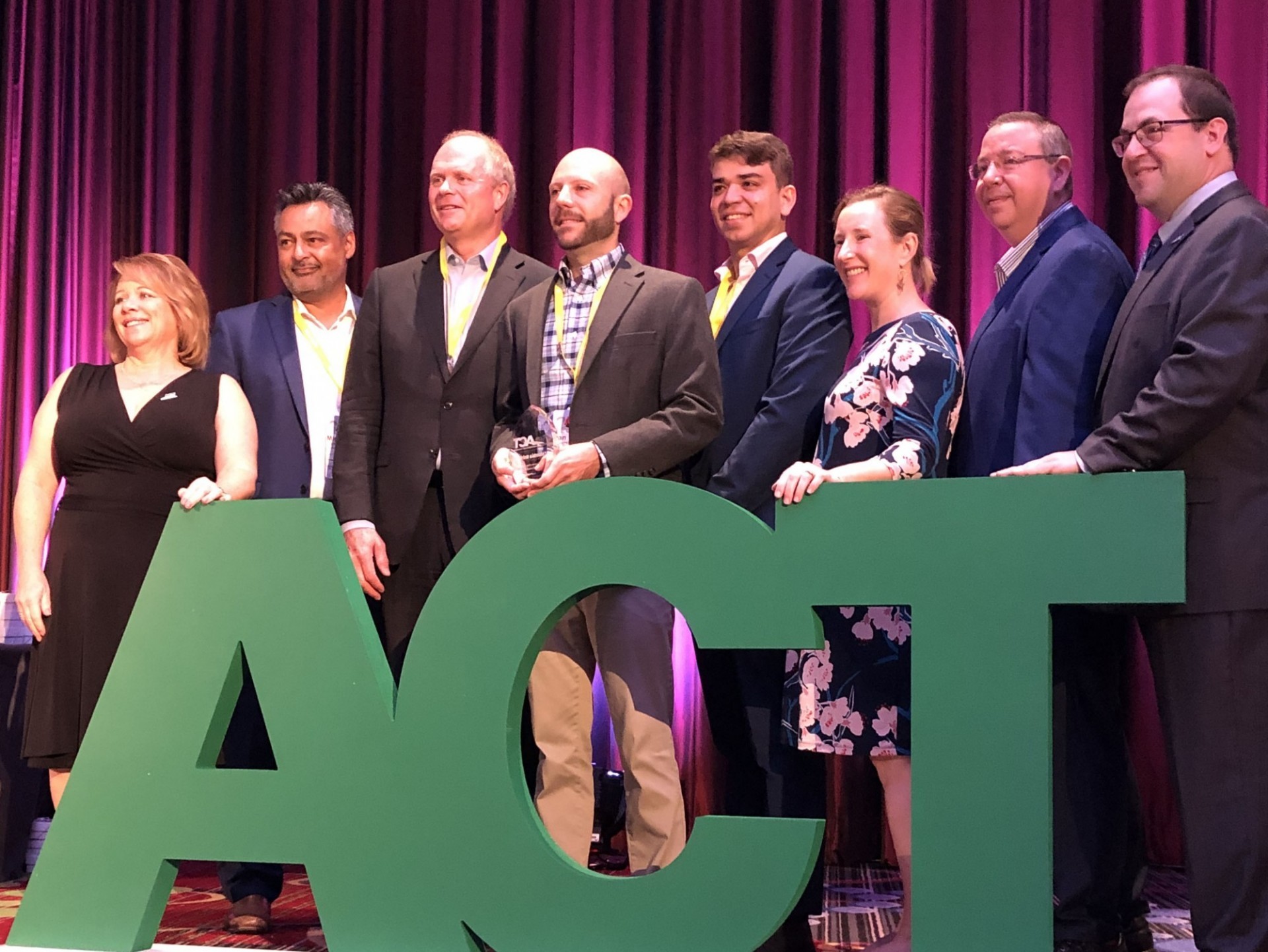  Columbia University representatives from the Transportation and Environmental Stewardship offices accept the award in front of large, green letters that read "ACT."