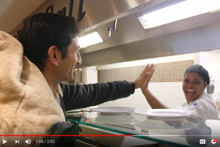 A man giving a high five to a Columbia Dining employee who is behind the counter working at her station.