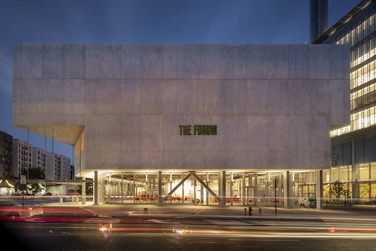 The side of The Forum building in the evening, with lights illuminated on the ground floor and a green sign that reads, "The Forum" in the middle of the facade.