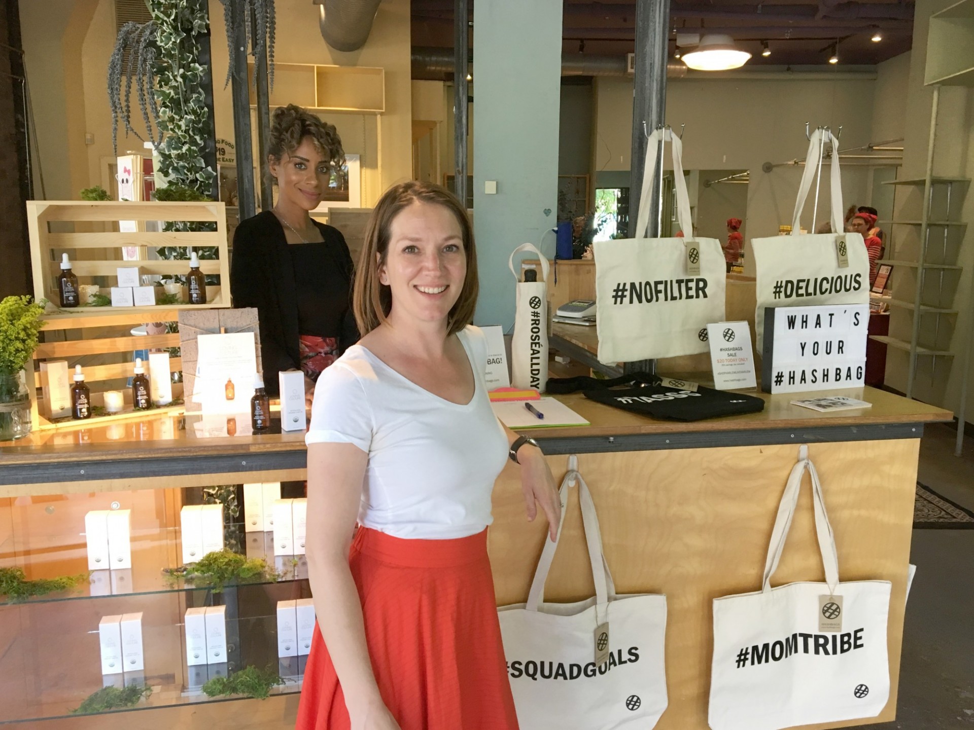 Two women stand by a booth that has hashtag totes and skincare products.