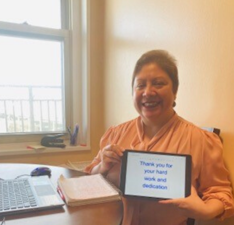 A woman sits at a round table holding an Ipad that reads, "Thank you for your hard work and dedication."