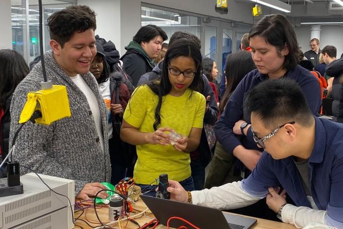 Students hover around a desk and examine something made in the Columbia Makerspace during the grand opening event